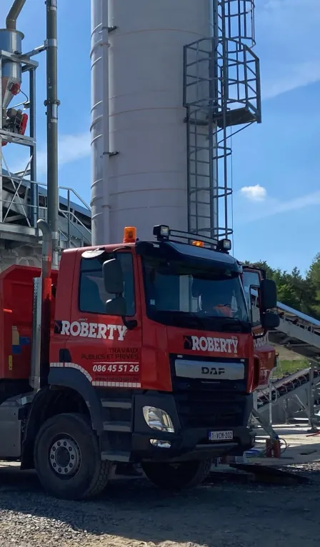 Red Roberty dump truck parked in front of a silo on a worksite